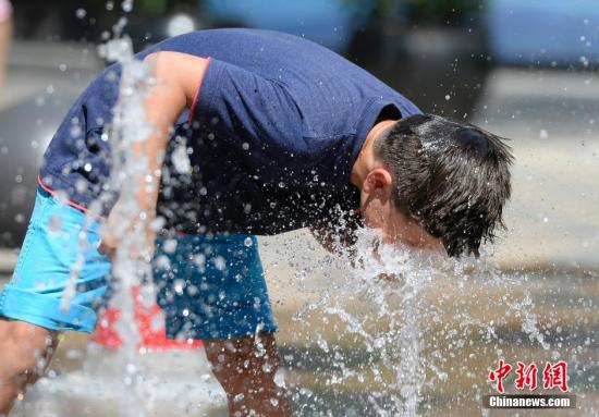 一名小孩將頭伸向北京街頭的噴泉以降溫祛暑