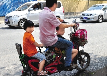 周先生騎著一輛低矮的電動車帶著一對兒女，很不安全。