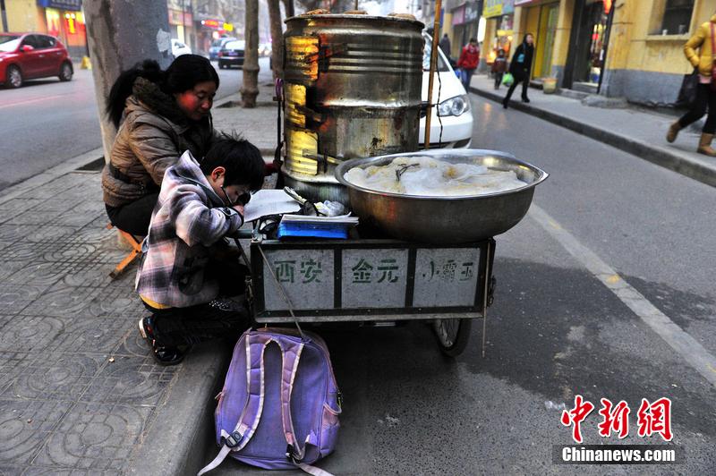 男孩西安路燈下寫作業(yè) 媽媽邊賣紅薯邊輔導(dǎo)