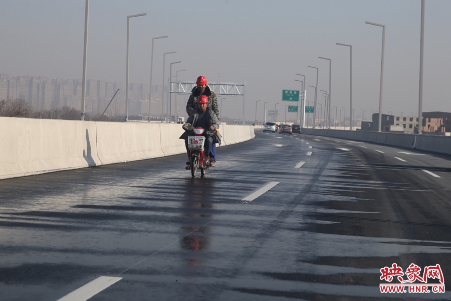 兩名工人騎車經過灑水養(yǎng)護路面。